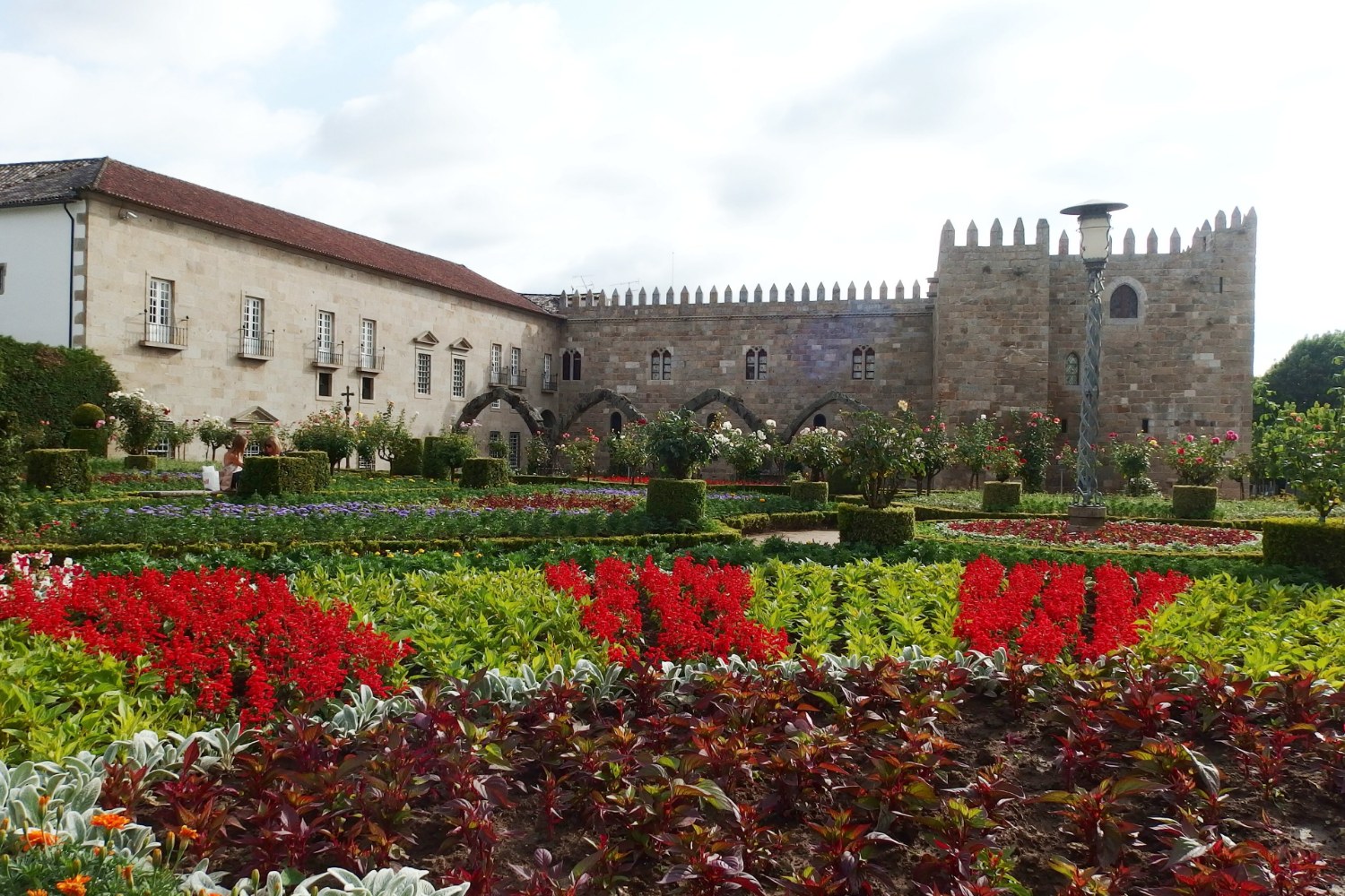 Jardim de Santa Bárbara com flores vermelhas e o Paço Episcopal ao fundo